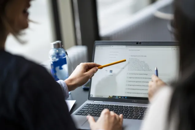 Students having a conversation by a laptop. Photo.